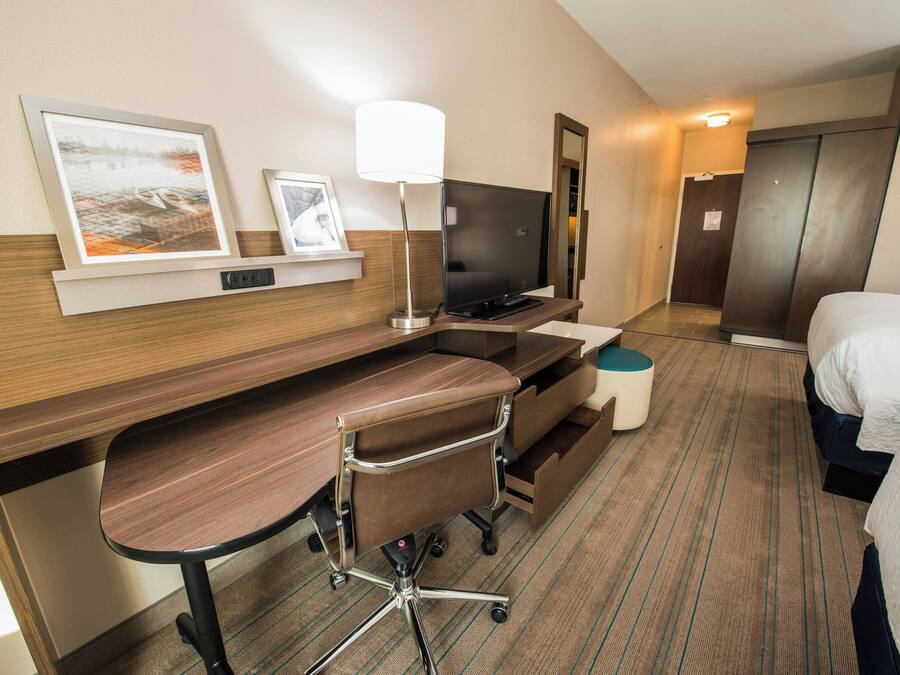A hotel room with a wooden desk, a chair, a television, a bed, and a small round table.
