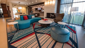 A modern hotel lobby with a curved blue sofa, a round coffee table, and a large window offering a view of the outside.