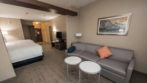 A hotel room with a bed, a sofa, two small tables, a TV, and a framed picture on the wall.