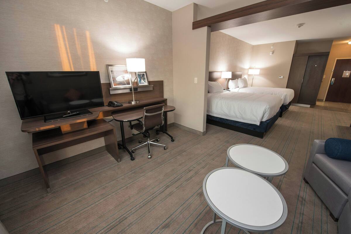 Ein Hotelzimmer mit einem Bett, einem Schreibtisch mit Stuhl, einem Fernseher und zwei kleinen Tischen.