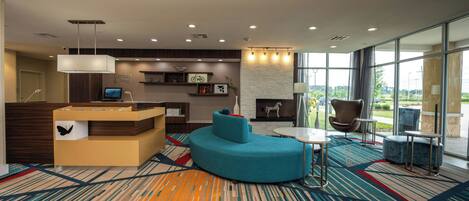 A modern lobby with a reception desk, seating area, and large windows offering a view.