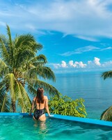 A person in a swimming pool with a view of the ocean and palm trees.
