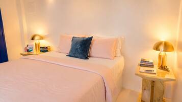 A hotel room with a bed, two bedside tables with lamps, a nightstand, and a small wooden side table with books and a notepad.