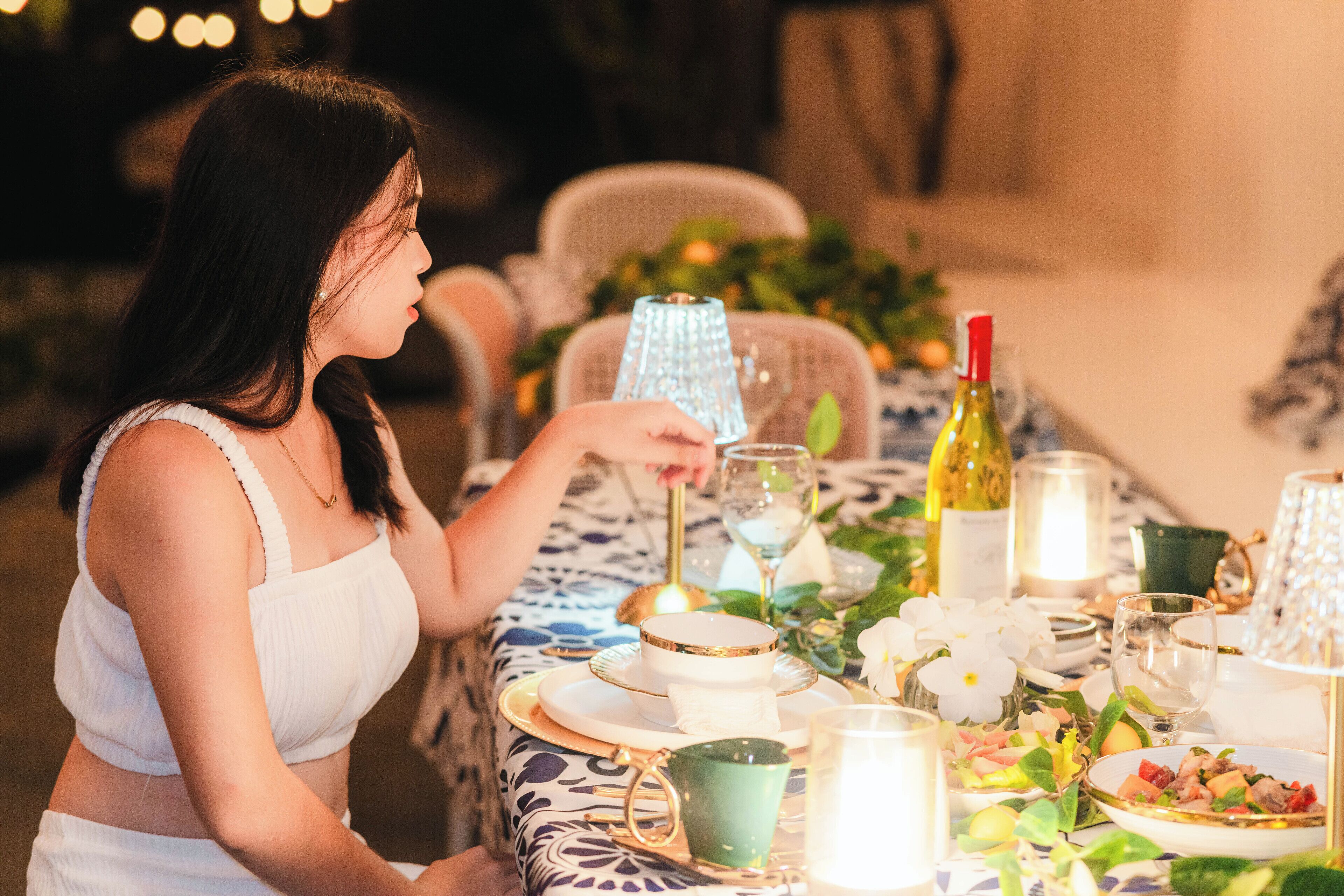 A dining table set with plates, glasses, and a bottle, surrounded by chairs and a decorative centerpiece.