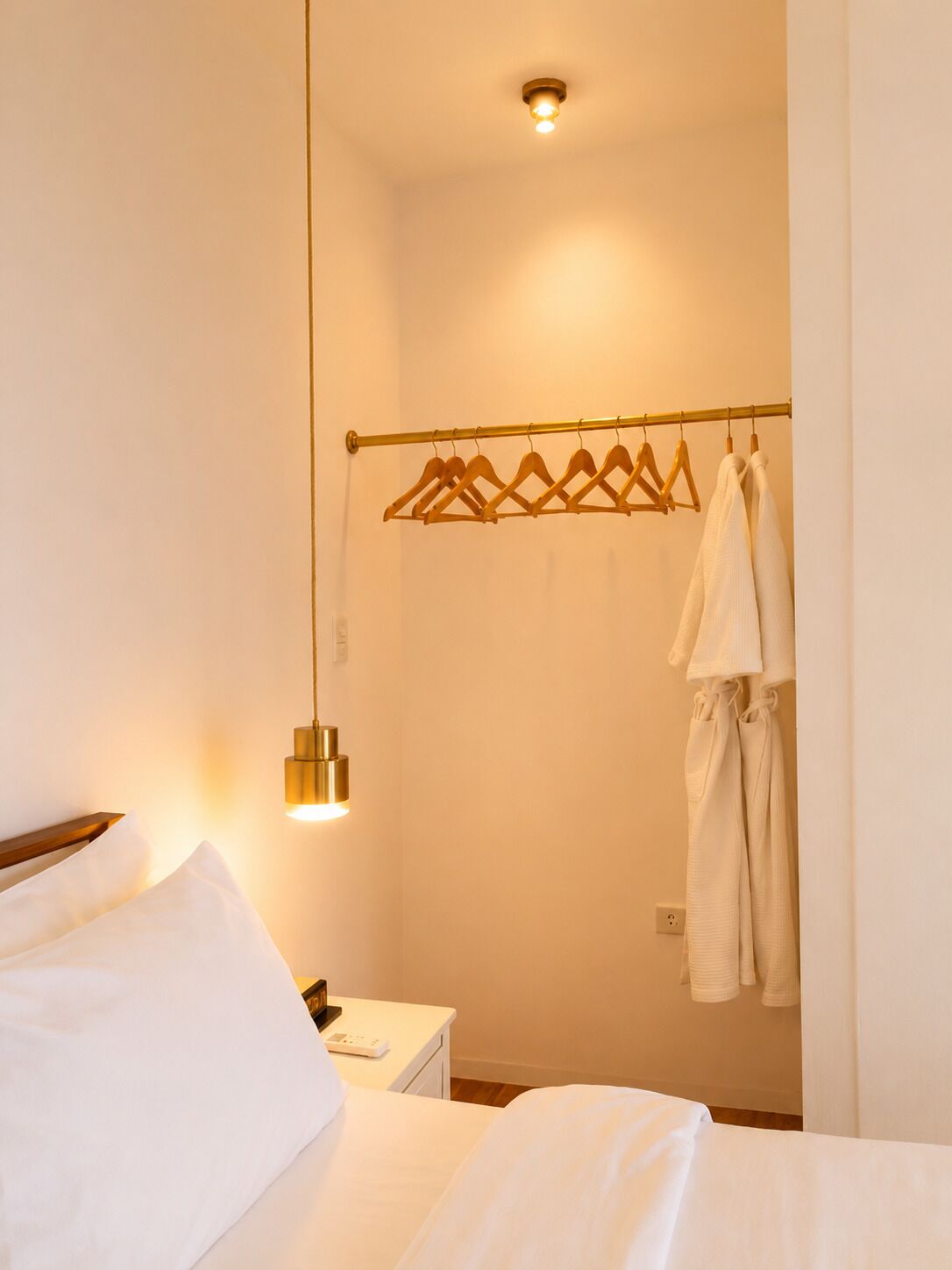 Habitación de hotel con cama, mesita de noche, perchero y lámpara fijada a la pared.