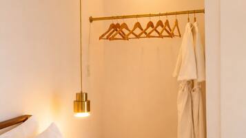 Habitación de hotel con cama, mesita de noche, perchero y lámpara fijada a la pared.