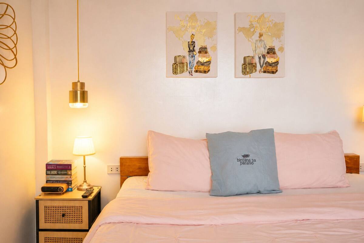 Un lit bien fait, avec deux oreillers, une lampe de chevet, une pile de livres et une carte du monde décorative accrochée au mur.