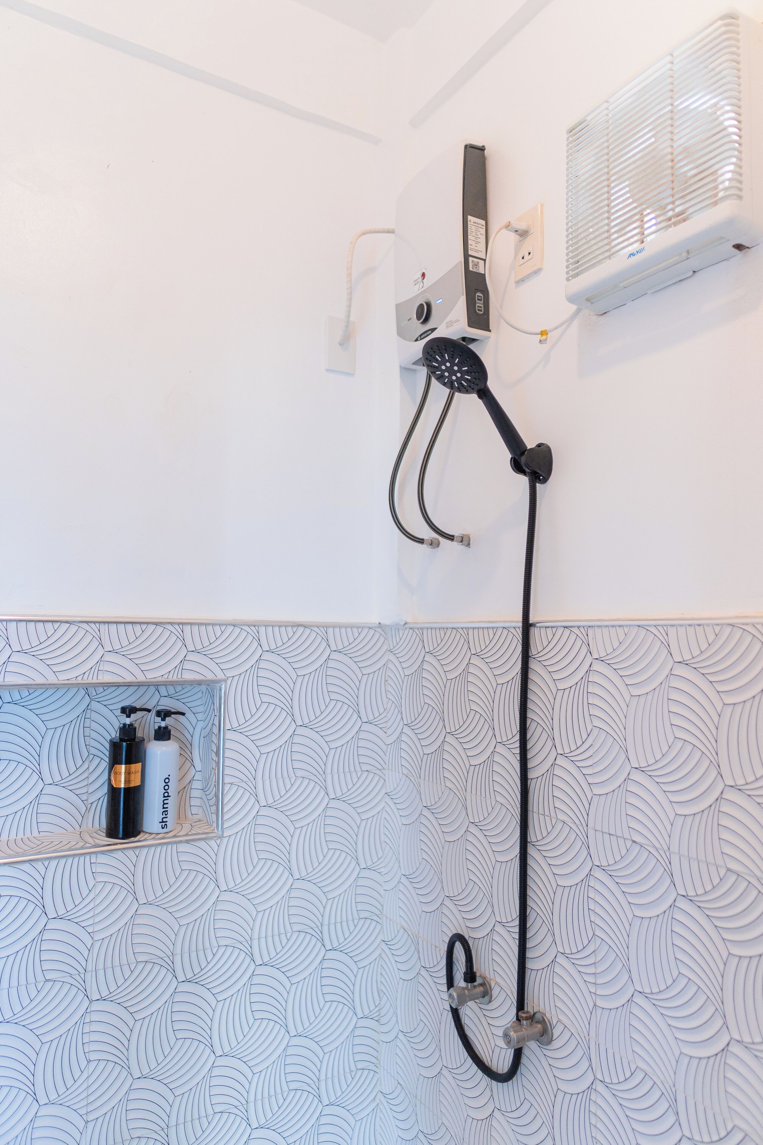 A shower with a handheld showerhead, a wall-mounted air conditioner, and a shelf with toiletries.