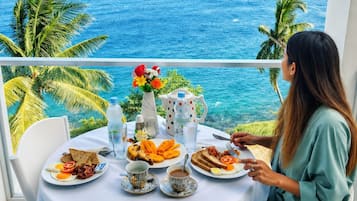 A woman dining at a table with a view of the ocean, plates of food, and a vase of flowers.