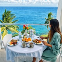 A woman dining at a table with a view of the ocean, plates of food, and a vase of flowers.