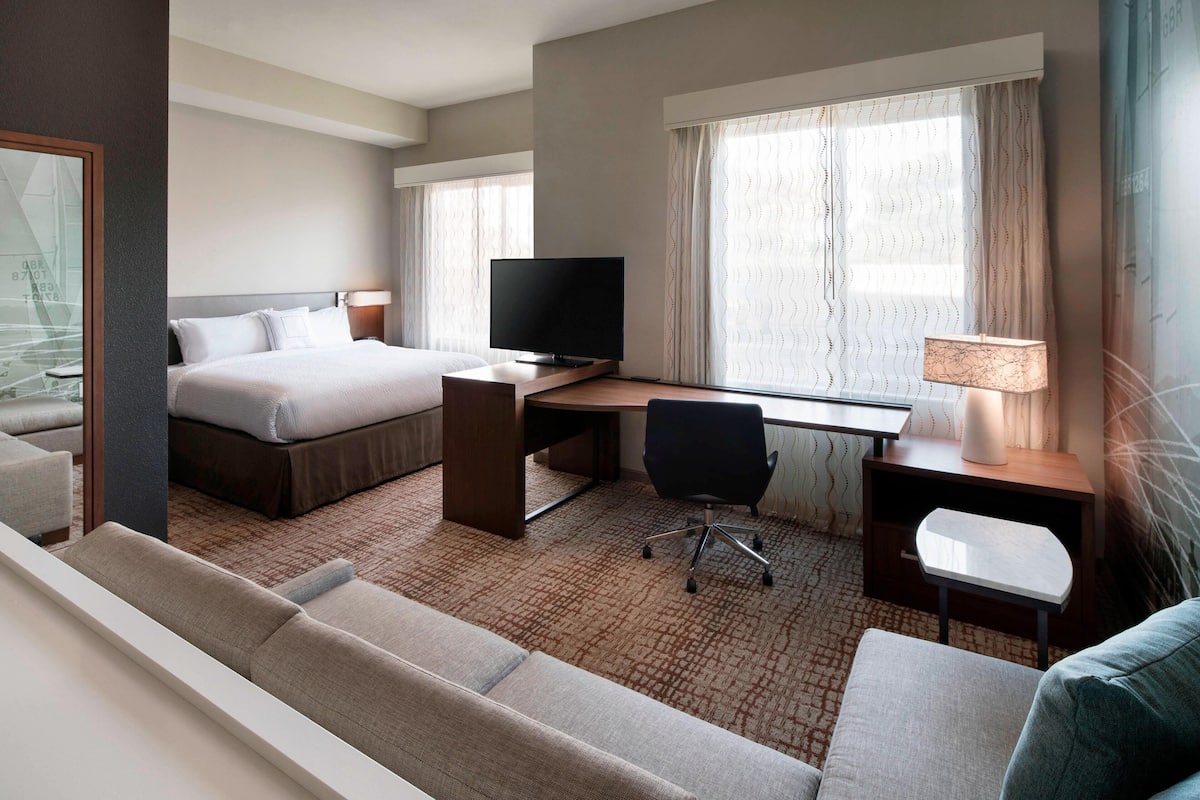 Habitación de hotel con cama, escritorio, televisor y zona de estar.