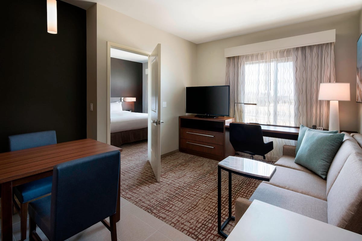 Habitación de hotel con comedor, sofá, televisor y ventana con cortinas.