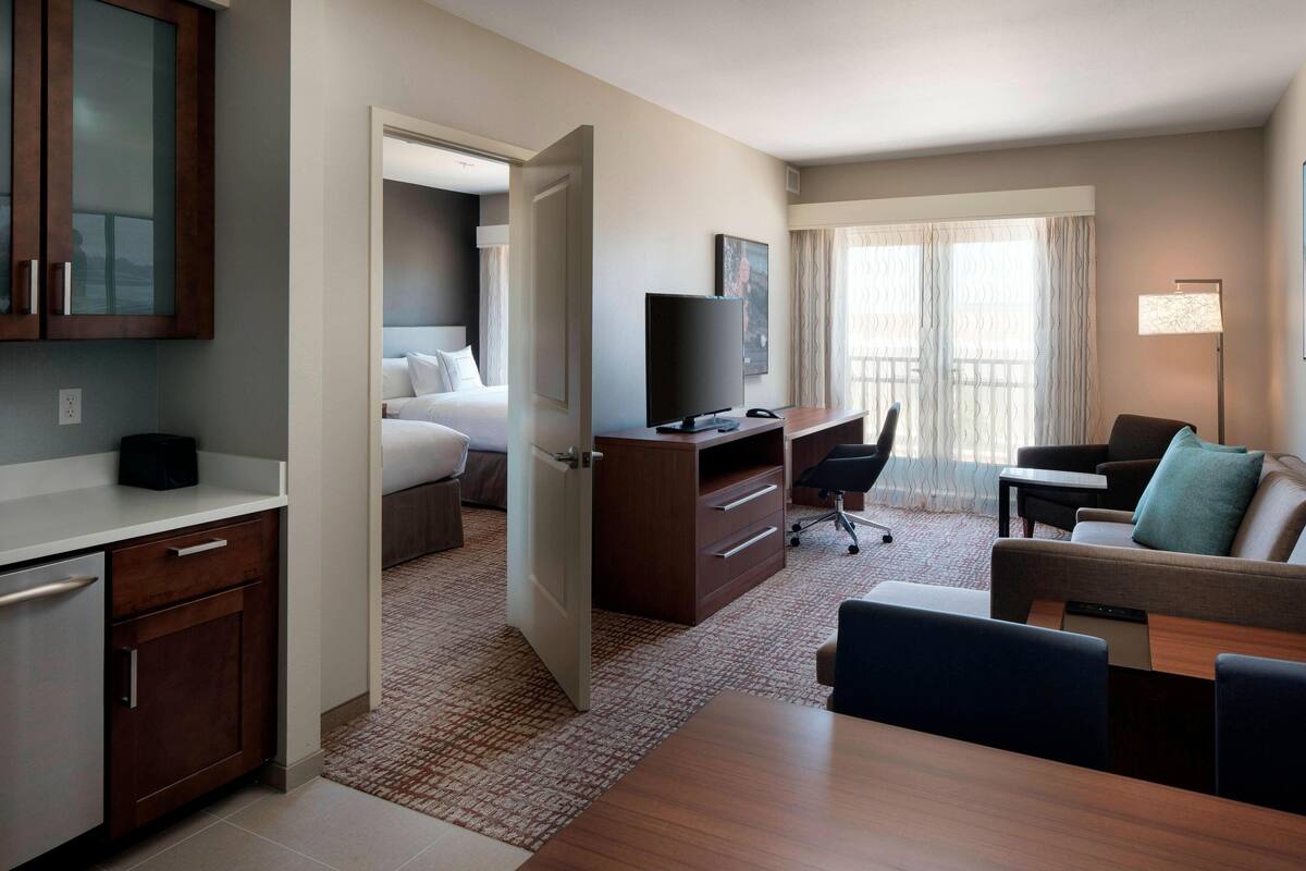 Habitación de hotel con una cama, un escritorio, una silla, un televisor y una ventana con cortinas.