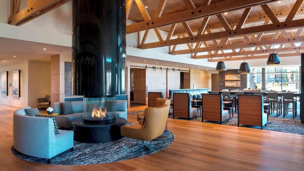 A spacious lobby with a high ceiling, a central fireplace, comfortable seating, and a dining area.