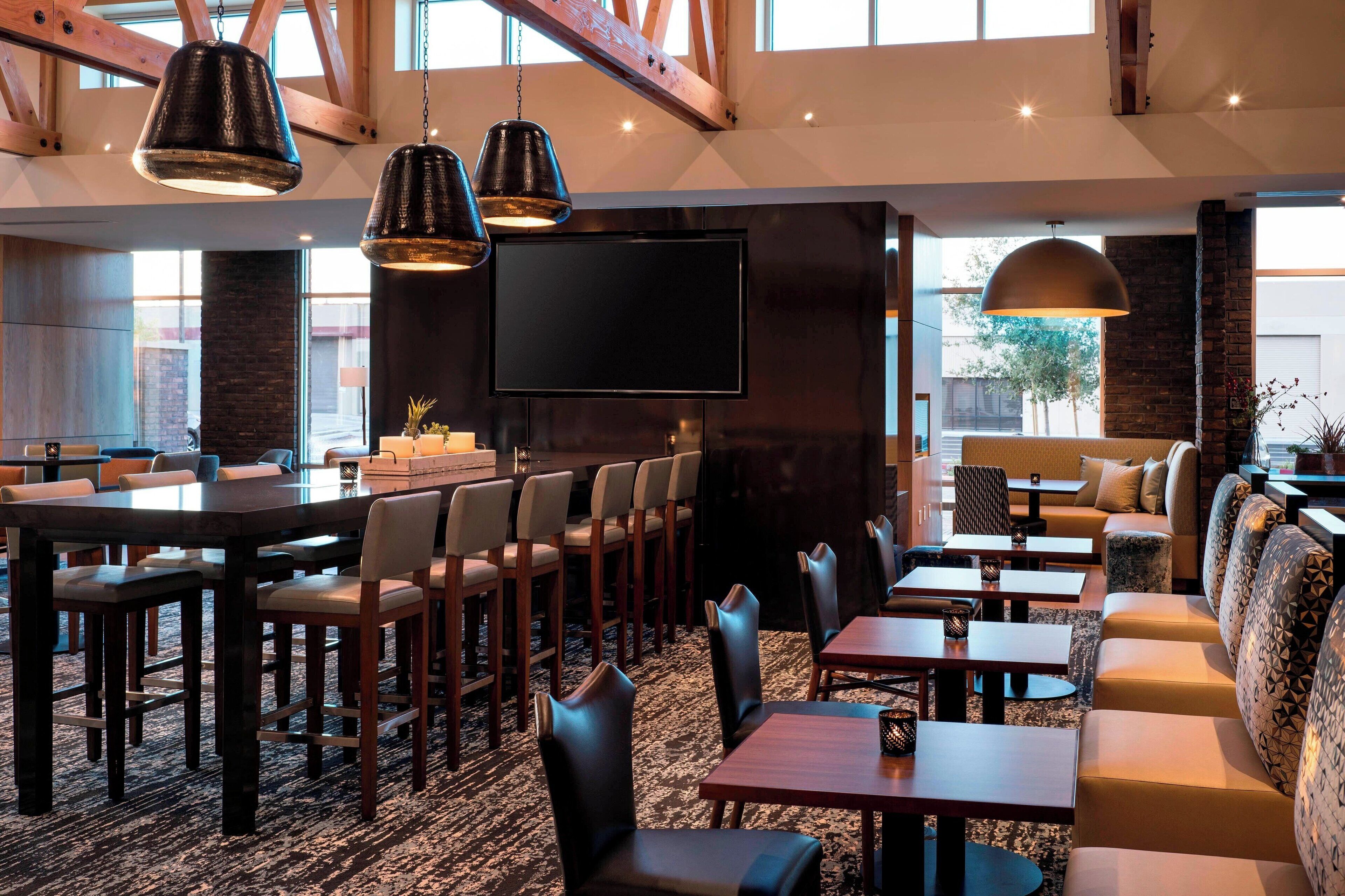 Un restaurant moderne doté de hauts plafonds, de poutres apparentes en bois et proposant différents types de sièges, notamment des tables, des chaises et des canapés.