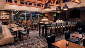 A spacious restaurant with high wooden beams, multiple seating areas including tables and booths, and a large TV screen.