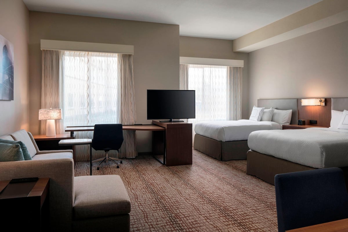 Habitación de hotel con cama, escritorio con televisor, una silla, un sofá y una lámpara.