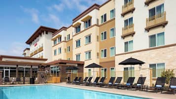 Un hotel con piscina, varios balcones y zonas de estar al aire libre.