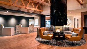 A modern lobby with a high ceiling, wooden beams, a central fireplace, and two armchairs.