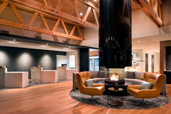 A modern lobby with a high ceiling, wooden beams, a central fireplace, and two armchairs. - Residence Inn by Marriott Redwood City San Carlos (San Carlos)