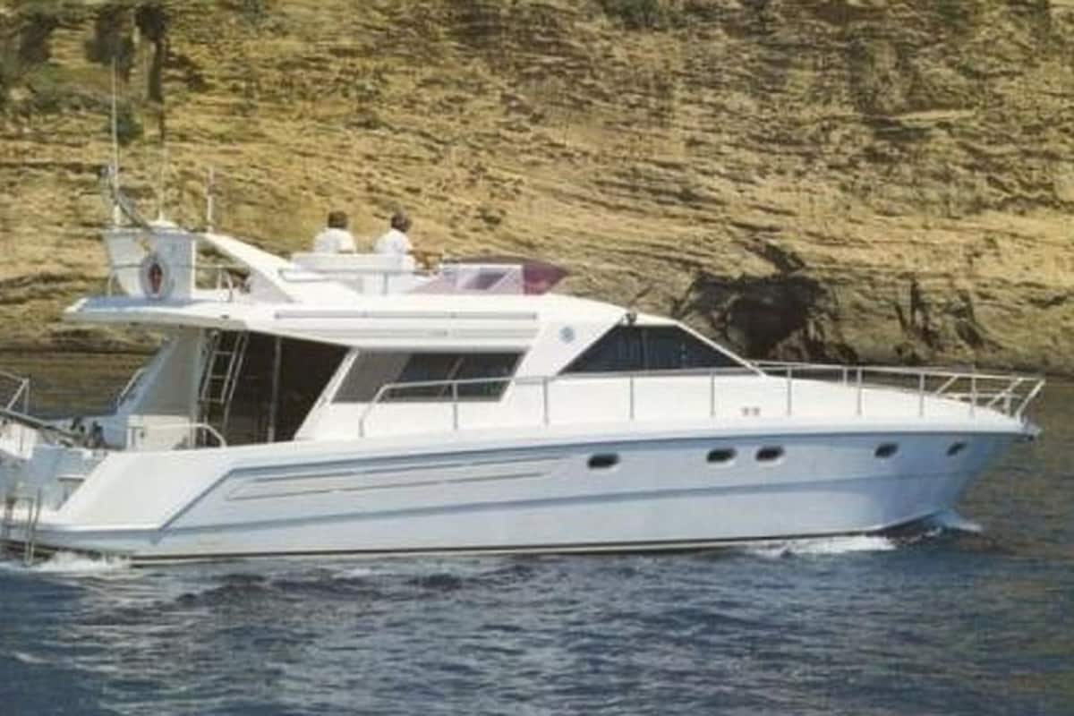 Eine weiße Yacht mit Kabine und Deck fährt auf dem Wasser, im Hintergrund ist eine felsige Küstenlinie zu sehen.