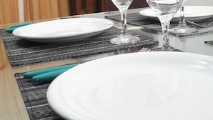 Ruokapöytä on katettu valkoisilla lautasilla ja kirkkailla viinilaseilla. Pöydällä on mustavalkoinen kuvioitu aluslauta ja seinällä riippuu kaupunkimaisemaa esittävä taulu.