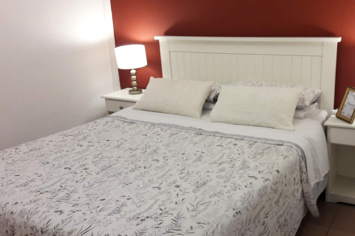 A neatly made bed with a floral-patterned bedspread, two pillows, and two bedside lamps on matching nightstands.