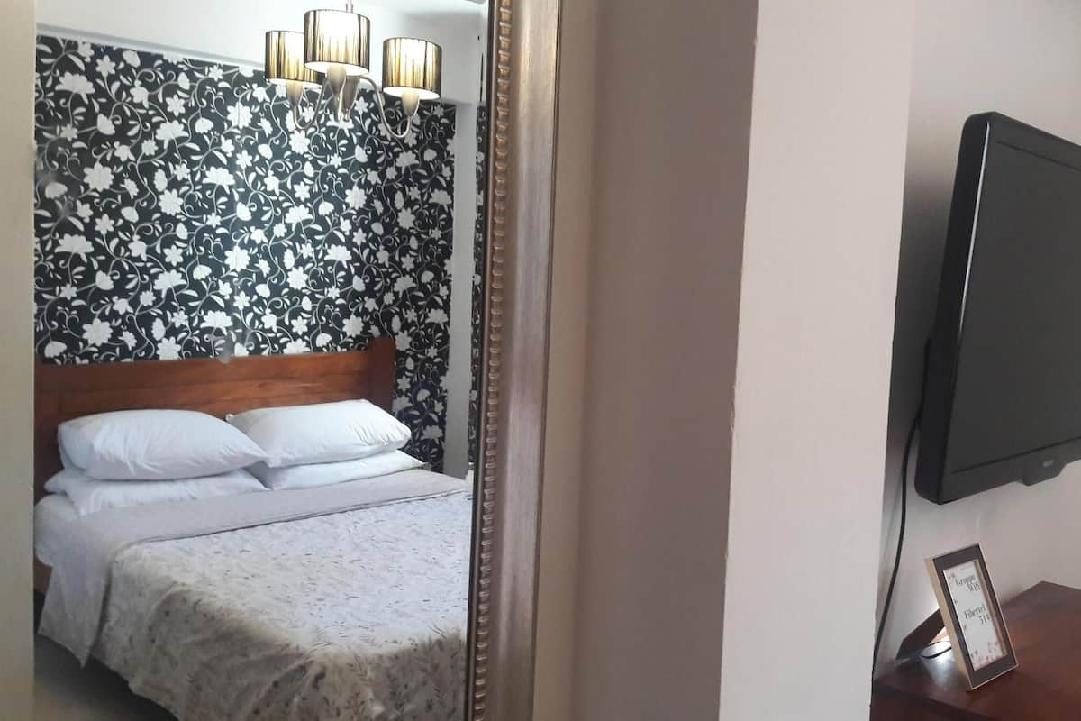 A hotel room with a bed, a television mounted on the wall, and a framed picture on a small table.