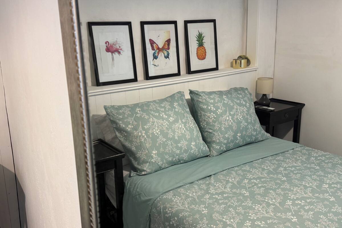 A bedroom with a bed, two pillows, a nightstand, a lamp, and three framed pictures on the wall.