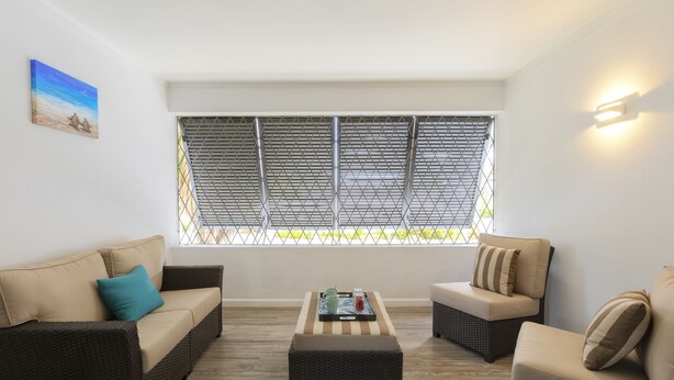 A room with two sofas, a coffee table, and a window with metal blinds. - Dover Woods Apartments (St. Lawrence Gap)