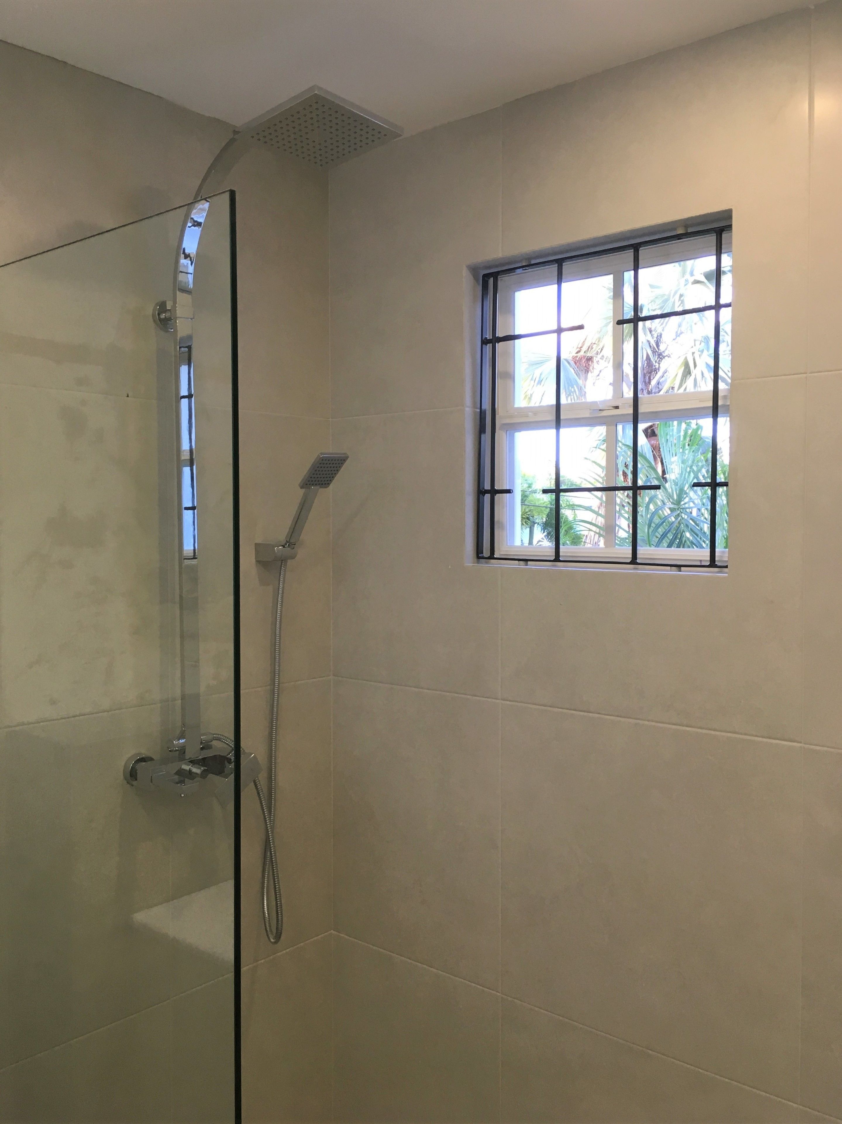 Een douche met glazen deur, een raam met uitzicht op groen en een betegelde wand.