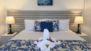 A neatly made bed with a floral-patterned bedspread, two matching pillows, and a towel with flowers. - Dover Woods Apartments (St. Lawrence Gap)