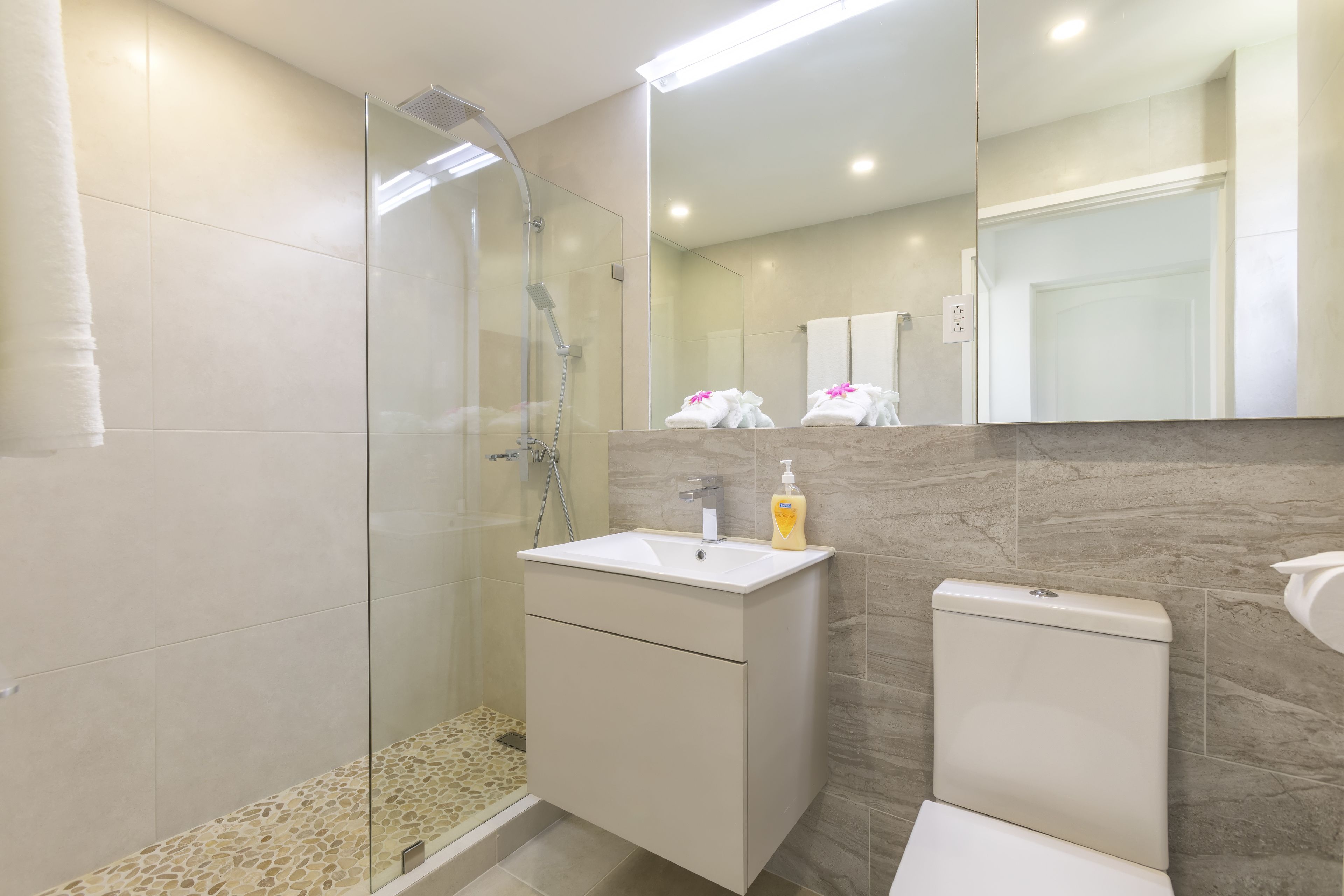 Un baño moderno con cabina de ducha de vidrio, un lavabo blanco y un inodoro.