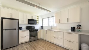 A modern kitchen with white cabinets, stainless steel appliances, and a large window providing natural light. - Dover Woods Apartments (St. Lawrence Gap)
