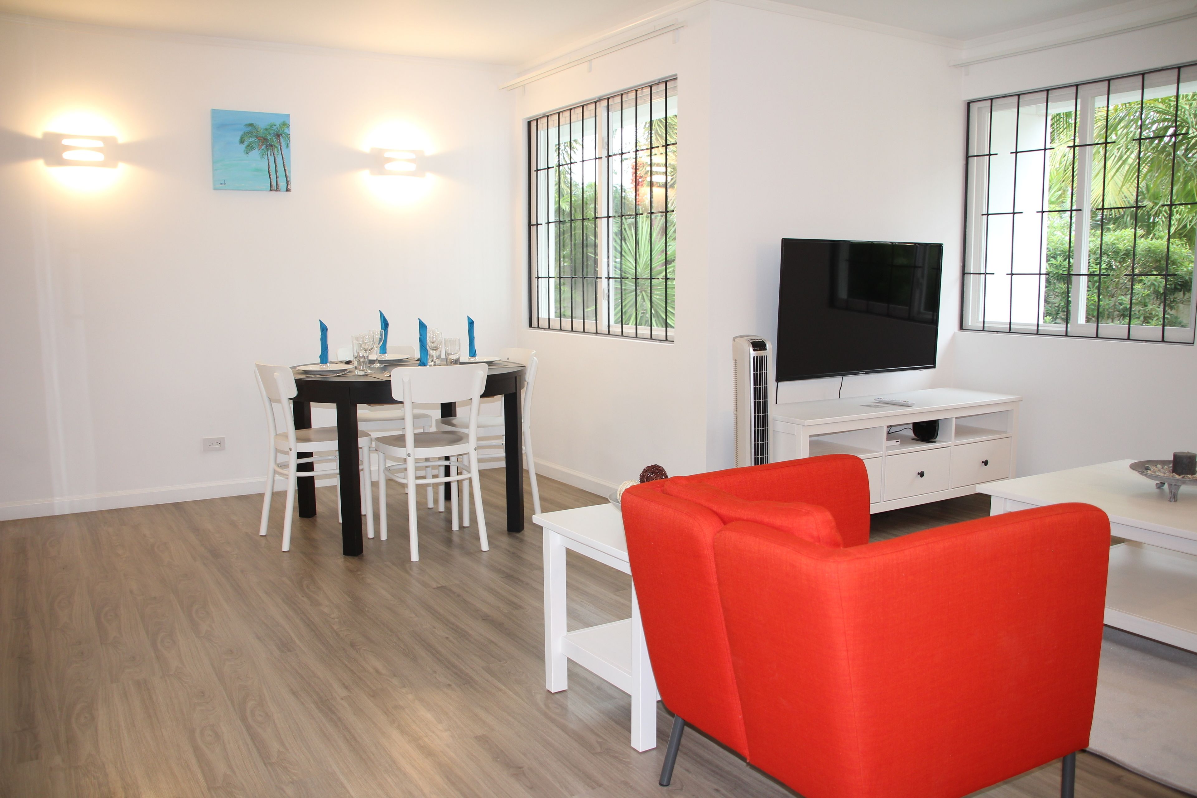A modern living room with a dining area, a TV, and a window with a view of greenery.