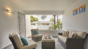A spacious balcony with wicker furniture, a small table, and a view of a building and trees. - Dover Woods Apartments (St. Lawrence Gap)