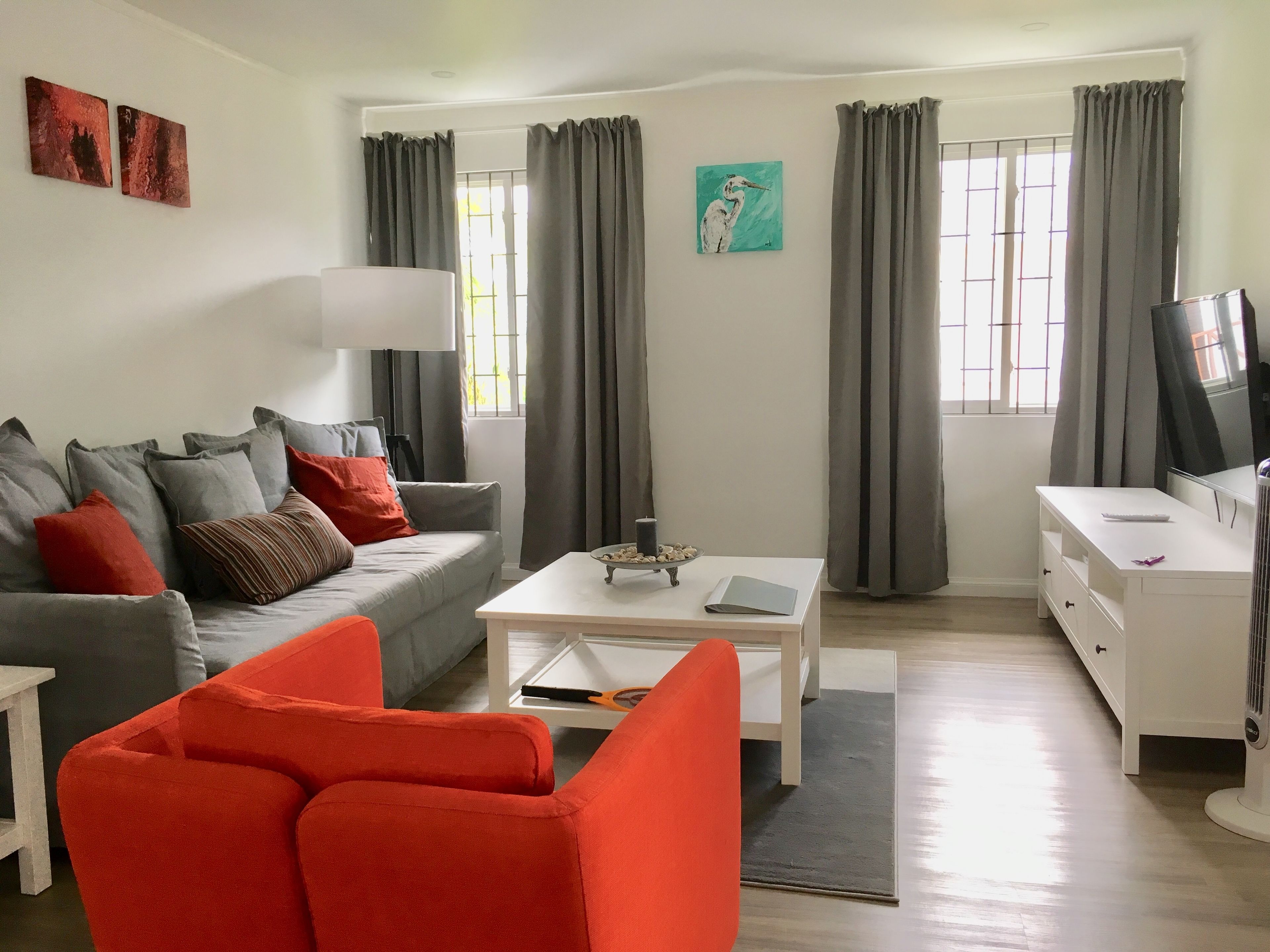 Una sala de estar moderna con un sofá gris, un sillón rojo, una mesa de centro blanca y un televisor sobre un mueble blanco.