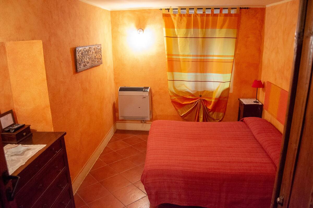 Quarto de hotel com uma cama, uma mesa de cabeceira com abajur, um ar condicionado fixado na parede e uma cortina.