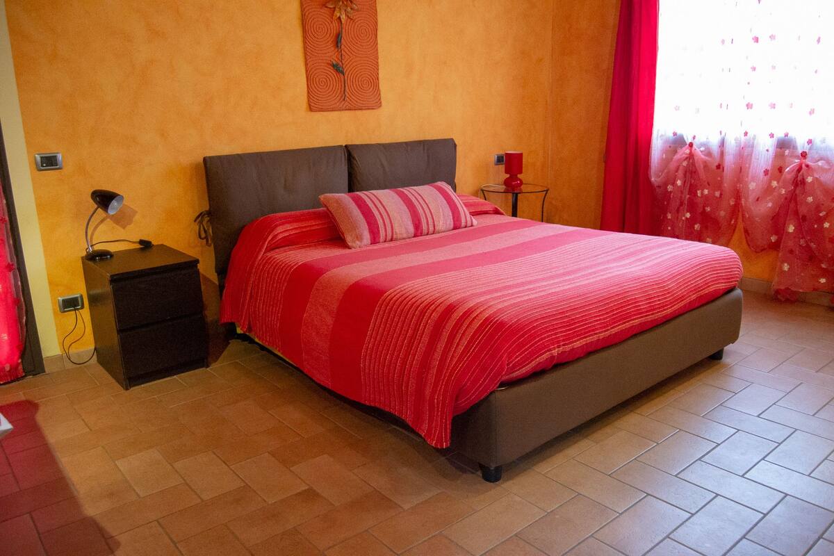 Quarto com uma cama grande, mesa de cabeceira, abajur e relógio de parede.
