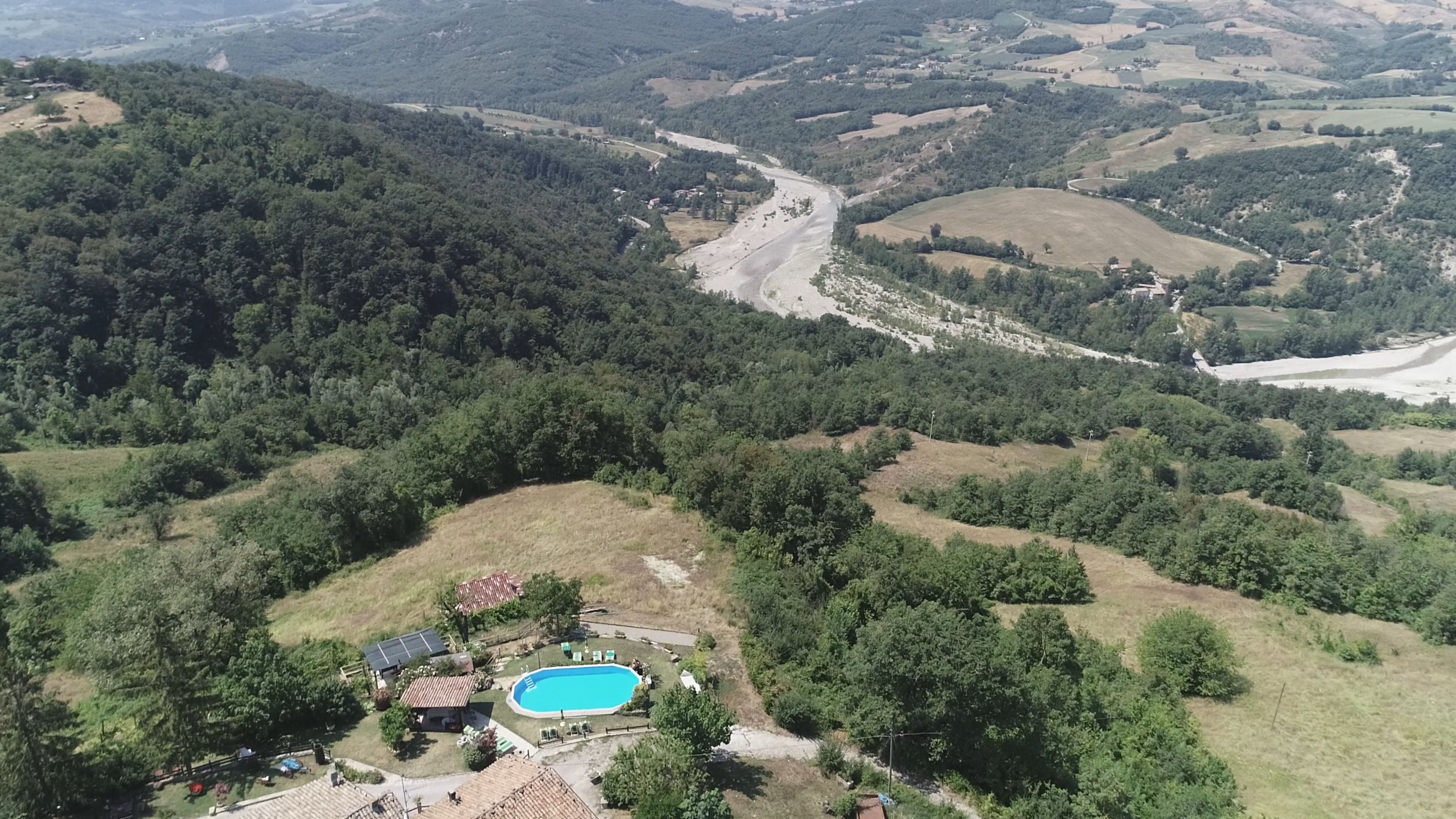 An aerial view of a rural area with a swimming pool, surrounded by lush greenery and hills.