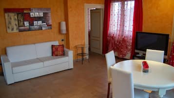 Un salon avec un canapé blanc, une petite table ronde et un téléviseur.