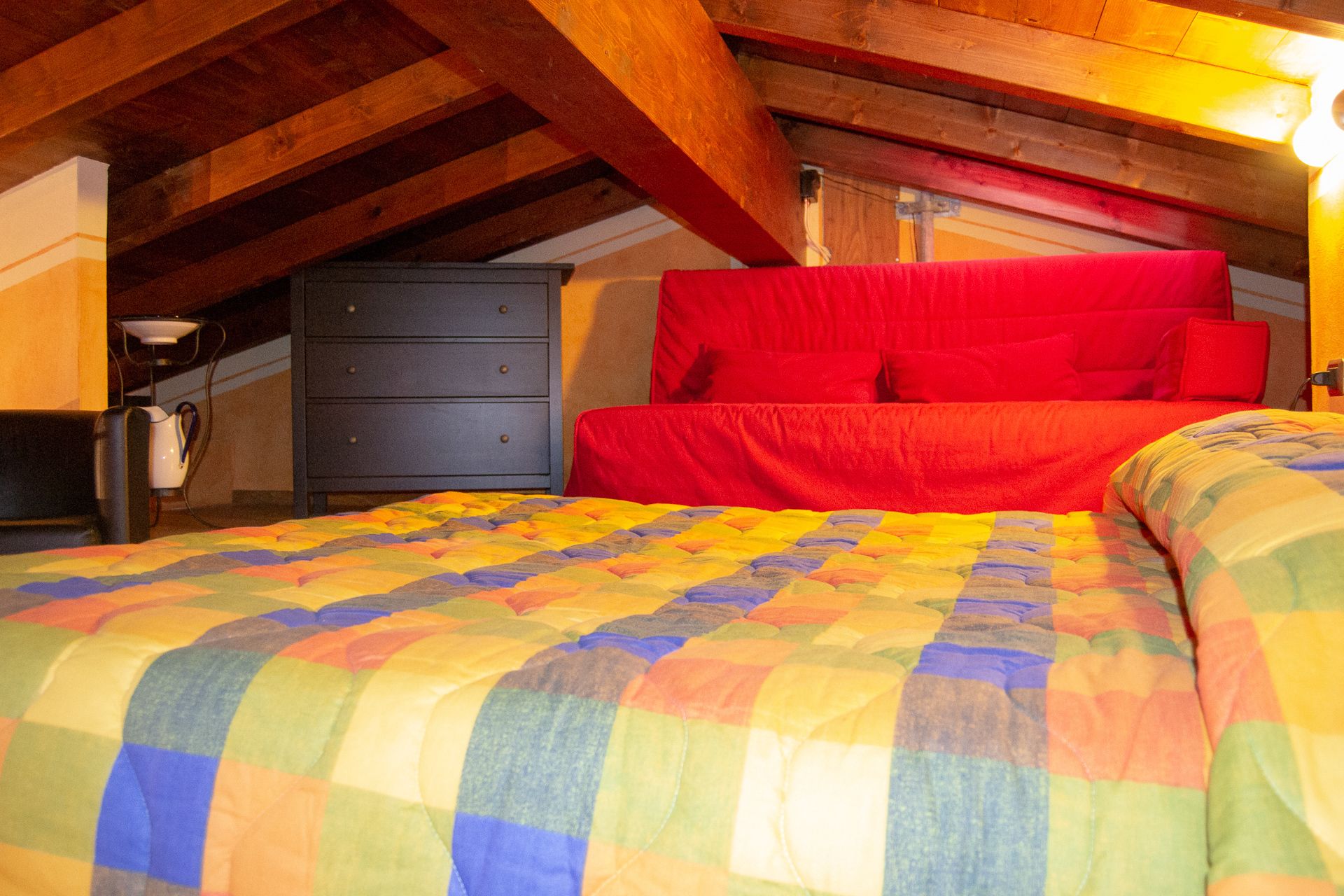 A bedroom with a colorful quilted bedspread, a red upholstered headboard, and a dark dresser.