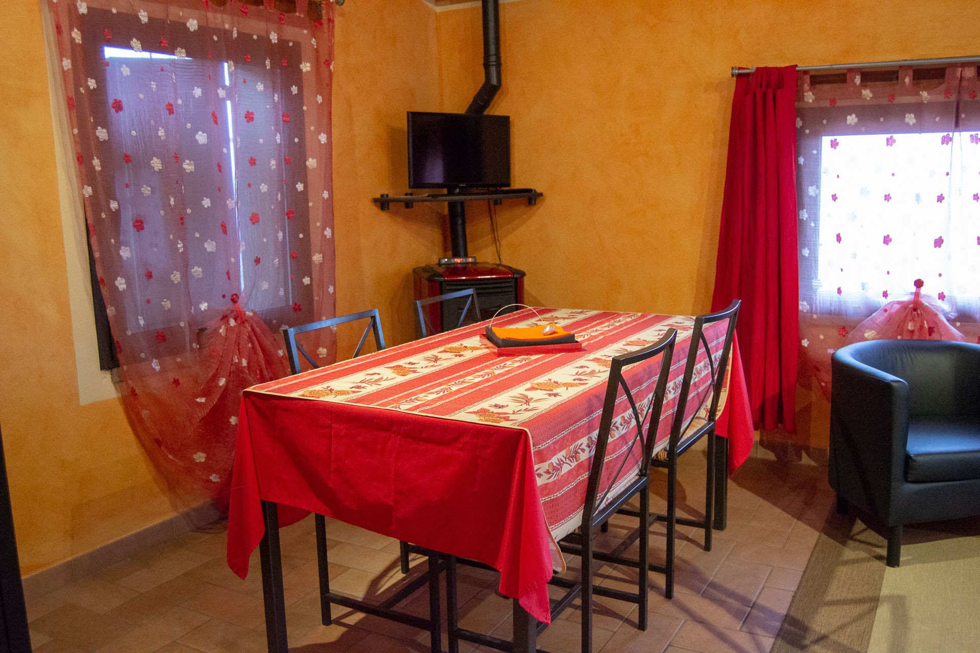 A dining area with a table covered in a red tablecloth, surrounded by chairs.
