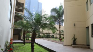 Ein Innenhof mit einer Palme, einem kleinen Garten und einem Gebäude mit Balkon.
