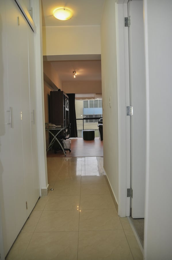 Un pasillo con piso de baldosas que conduce a una habitación con escritorio, silla y una mesita.