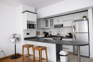 Une cuisine moderne avec des meubles blancs, un plan de travail noir, un four à micro-ondes encastré, une cuisinière et une poubelle.