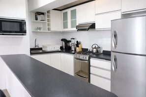 Une cuisine moderne avec des meubles blancs, un réfrigérateur en acier inoxydable, une cuisinière à gaz et un four à micro-ondes.