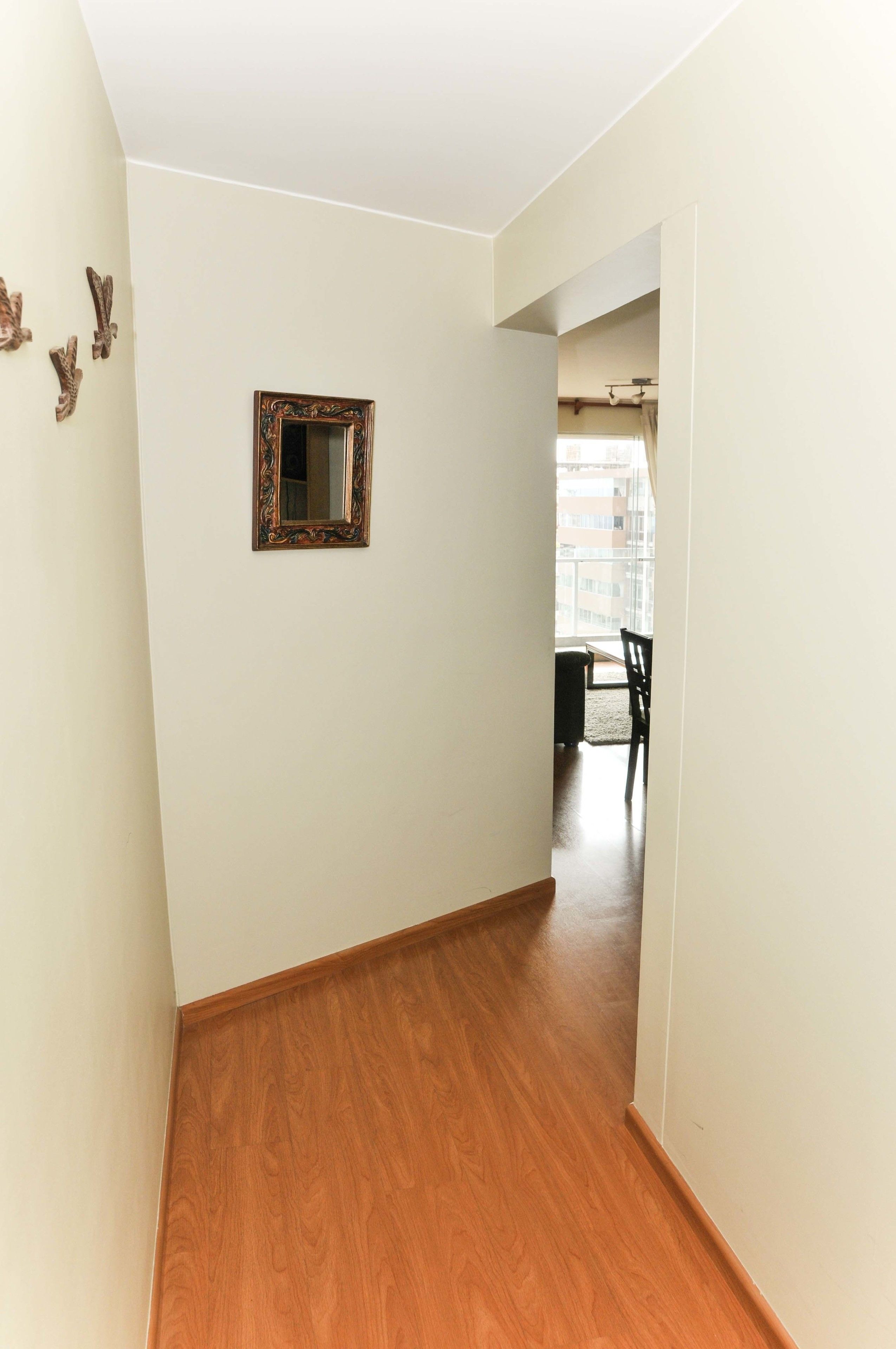 Un pasillo con suelo de madera, un espejo en la pared y vista a otra habitación con una mesa y sillas de comedor.