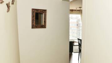 Un pasillo con suelo de madera, un espejo en la pared y vista a otra habitación con una mesa y sillas de comedor.