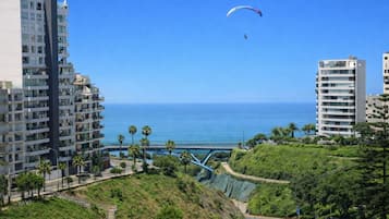 Un paisaje urbano costero con modernos rascacielos, un cielo azul despejado y una persona practicando parapente.